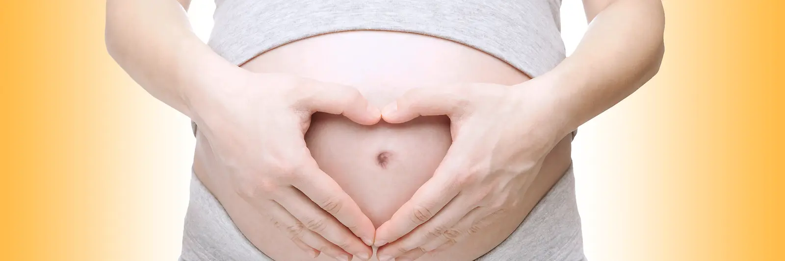 Hände formen ein Herz auf dem Bauch einer schwangeren Frau