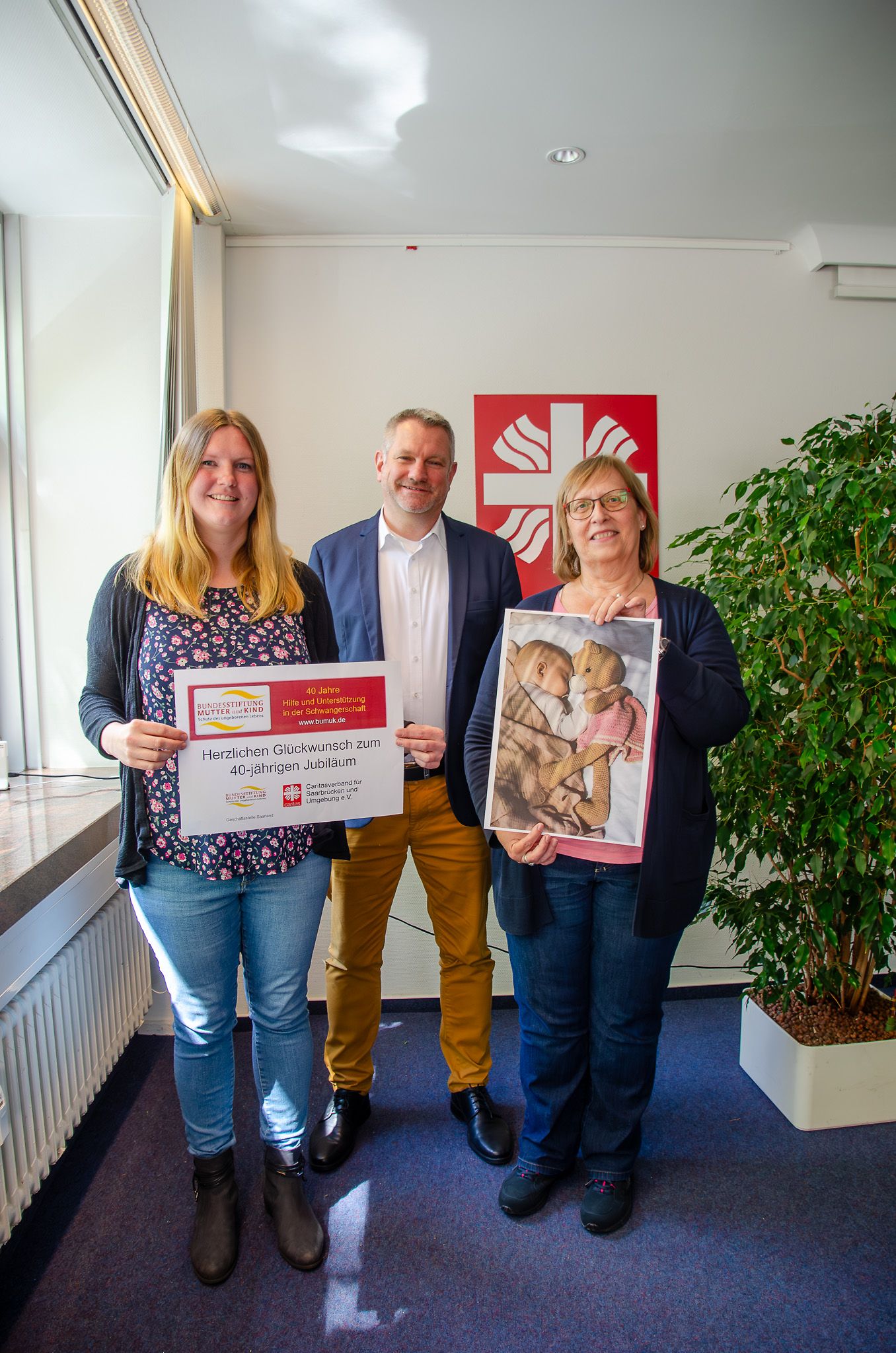 Zwei Frauen und ein Mann halten ein Schild mit der Aufschrift Herzlichen Glückwunsch zum 40-jährigen Jubiläum